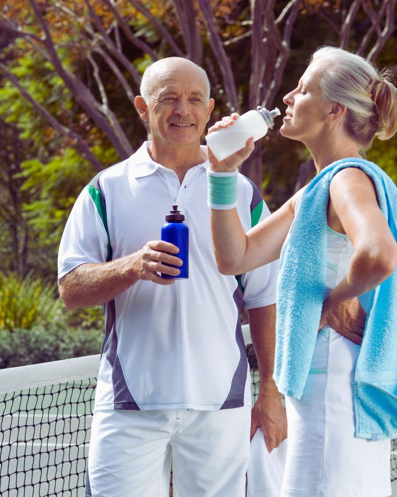 a man and woman drinking water after playing tennis