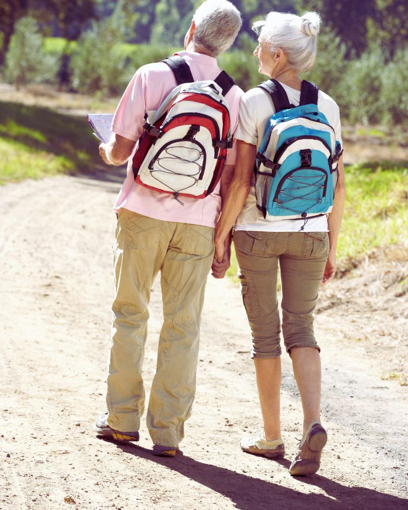 a man and woman holding hands and walking on a dirt path after discovering hobbies for couples over 50