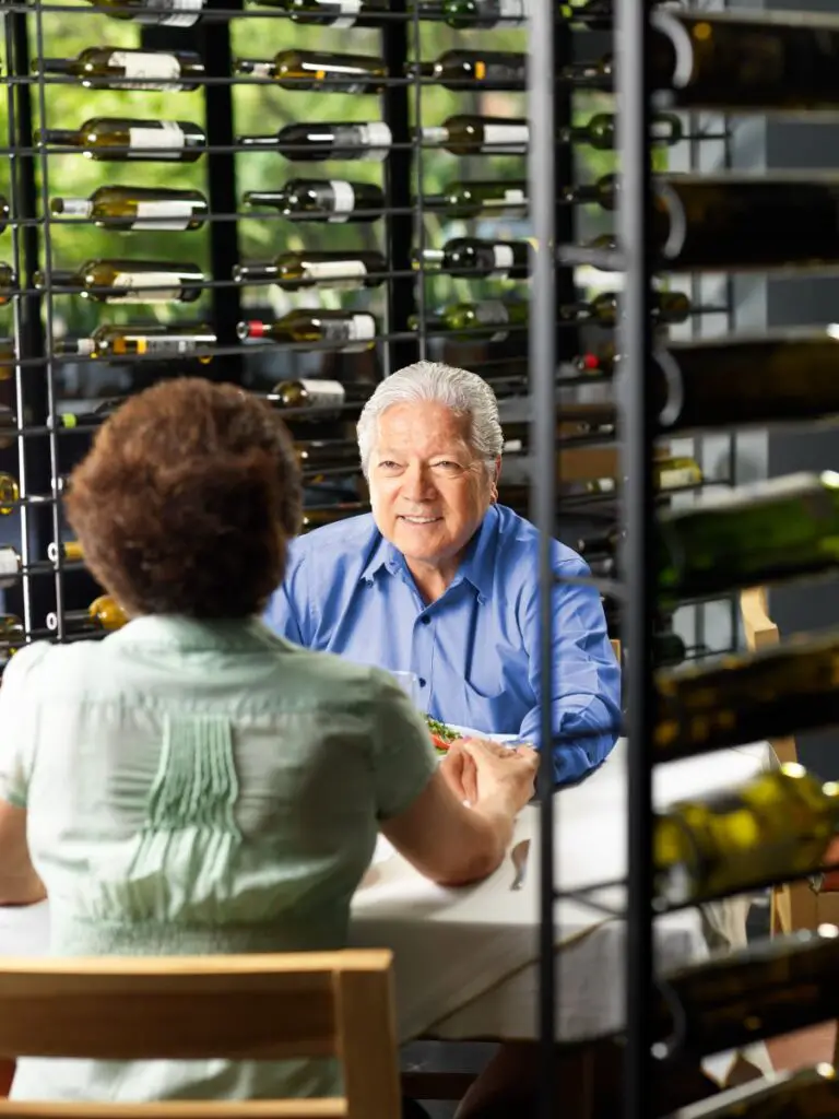 A man and woman sitting at a table with wine bottles behind them while on a date after seeing dating profile examples for females over 50.