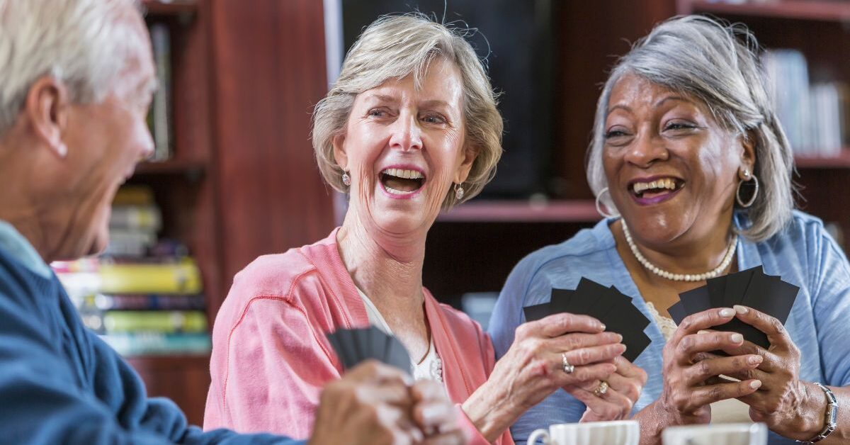 A group of women laughing and playing cards to demonstrate how important hobbies for people over 50 are.