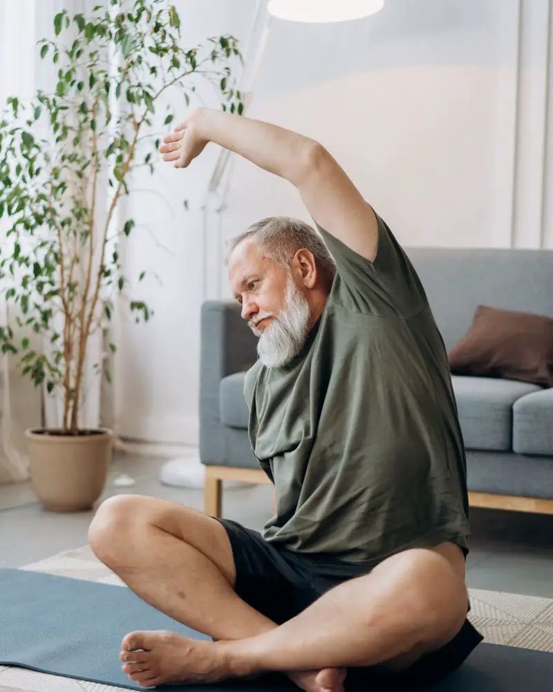 a man sitting on a mat stretching his arms to demonstrate safe stretches for people over 50