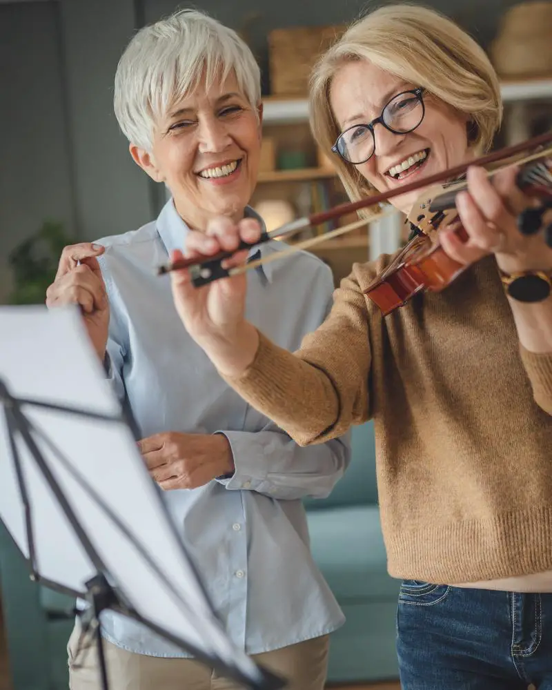 A woman playing violin through the instruction of another woman is using her musical talents as a side hustle over 50.