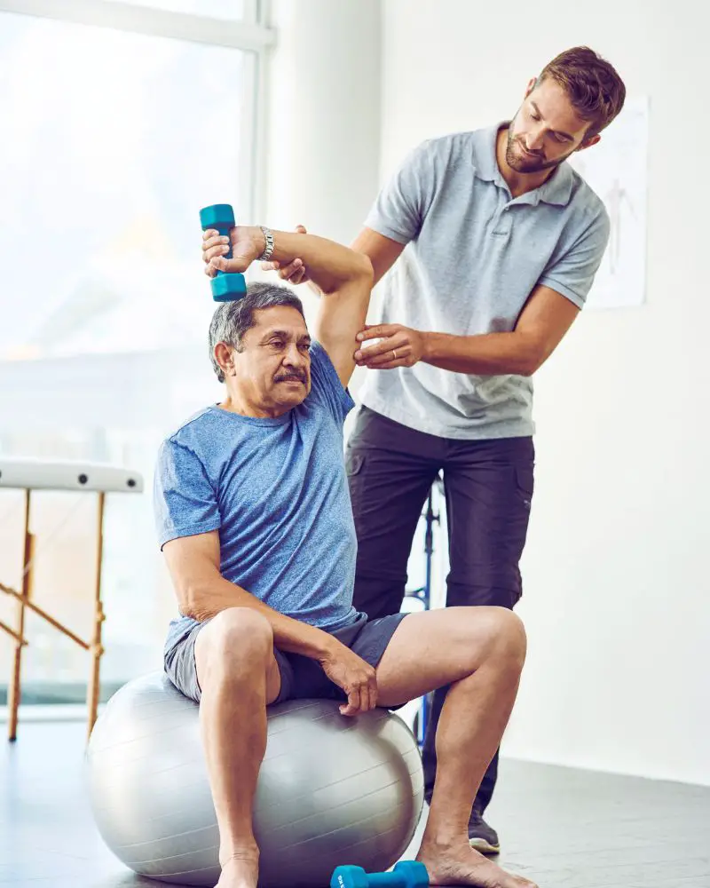 a man sitting on a ball with a dumbbell on his shoulder to demonstrate one of many interesting facts about physical therapy