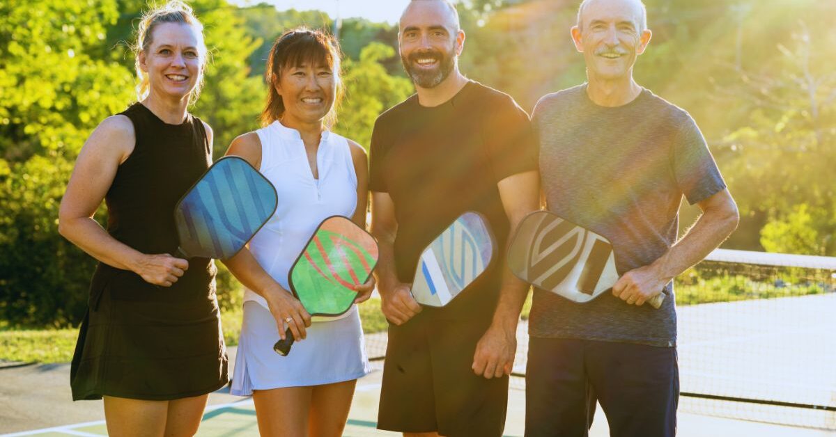 Group of four adults ready to use pickleball etiquette on the court.