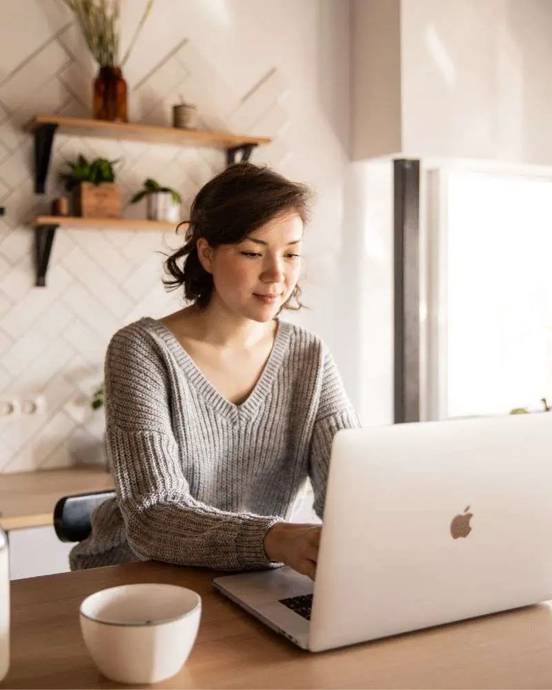 a woman sitting at a table using a laptop to write a blog and learn the best ways for bloggers to dominate SEO