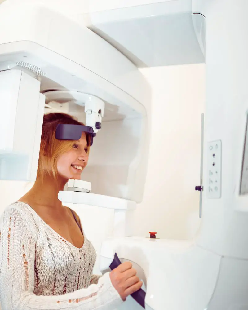 Woman standing getting a wrap around head dental xray to demonstrate one of many interesting facts of x-rays