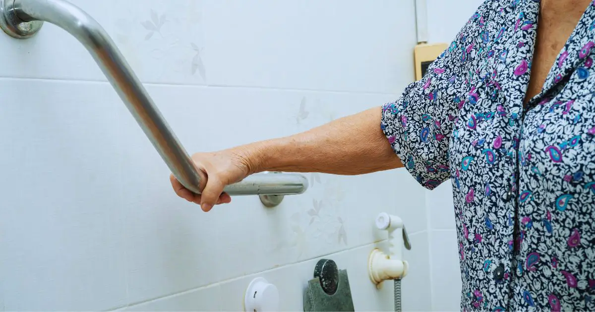 elderly woman holding a grab bar in the shower to demonstrate how often the elderly should shower for their health.