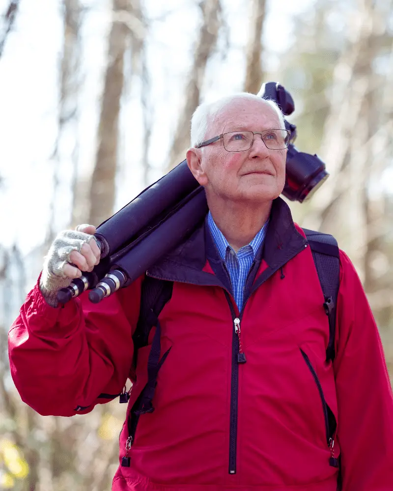 a man in a red jacket carrying a tripod to go birdwatching with couples over 50