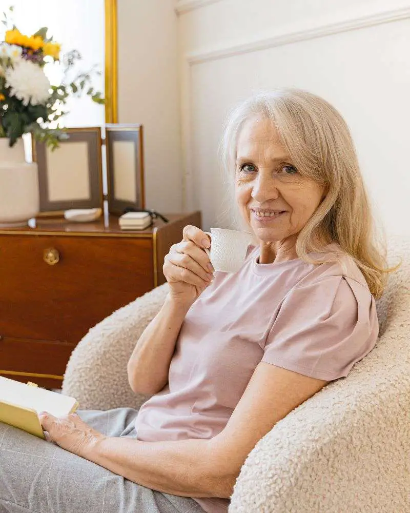 a woman sitting in a chair holding a cup and a book