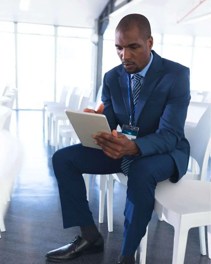 a man in a suit and tie sitting on chairs using a tablet reviewing how to write a retirement speech