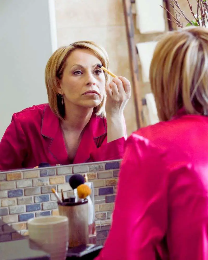 a woman applying makeup in front of a mirror after reading beauty bloggers for over 50