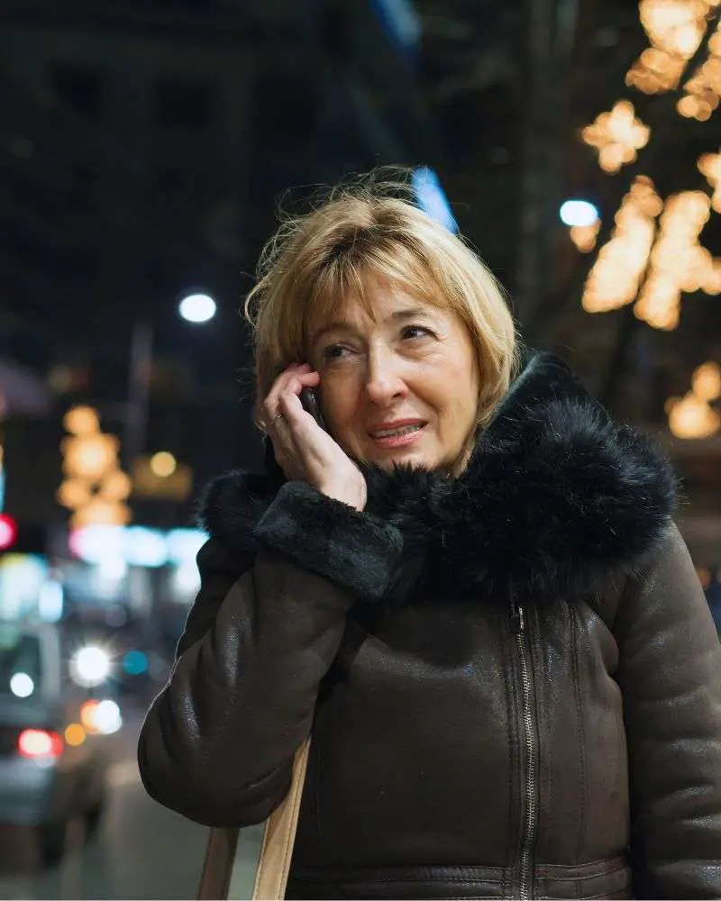 a woman talking on a cell phone calling a taxi because she is over 50 and afraid to drive