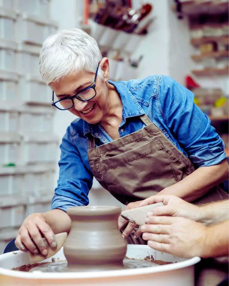 a woman in an apron painting a vase