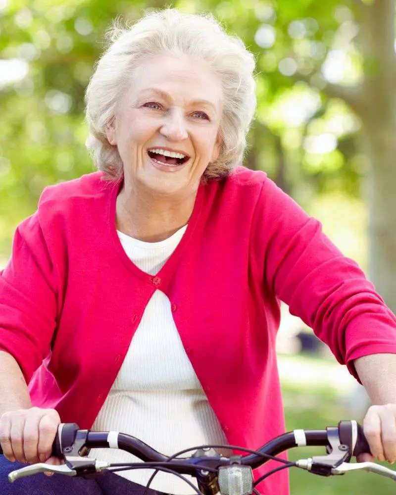 a woman smiling at camera while riding a bicycle after considering the pros and cons of not renewing your driver's license