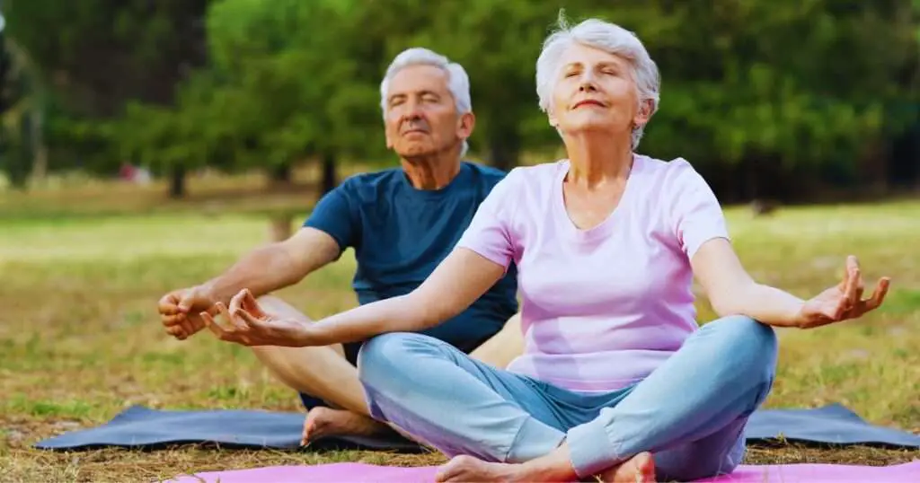 a man and woman sitting on the ground with their hands in the air demonstrating yoga for couples over 50