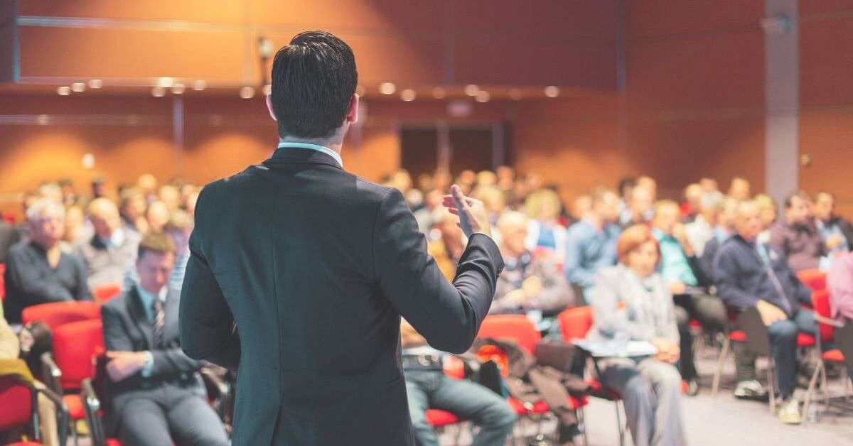 a man in a suit standing in front of a group of people after learning how to write a retirement speech