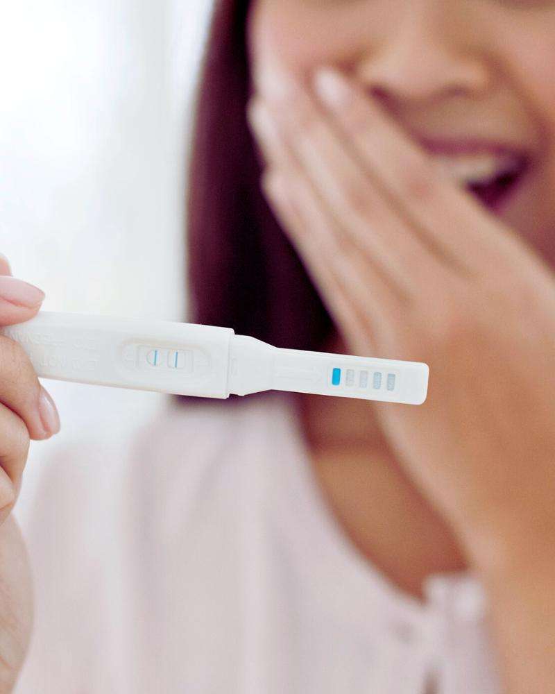 Woman smiling while looking at the results of a pregnancy test and probably wondering about pregnancy at 43 statistics 