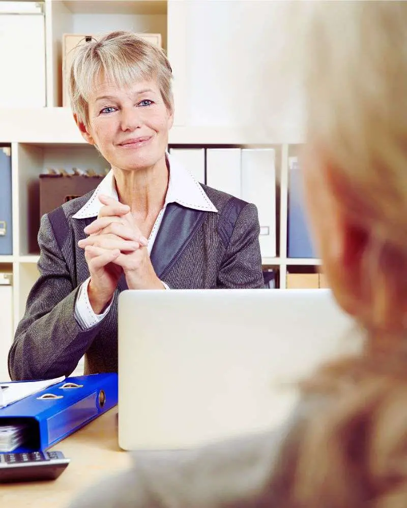 a woman sitting at a desk with her hands folded listening to someone who has been considering second careers for lawyers over 50