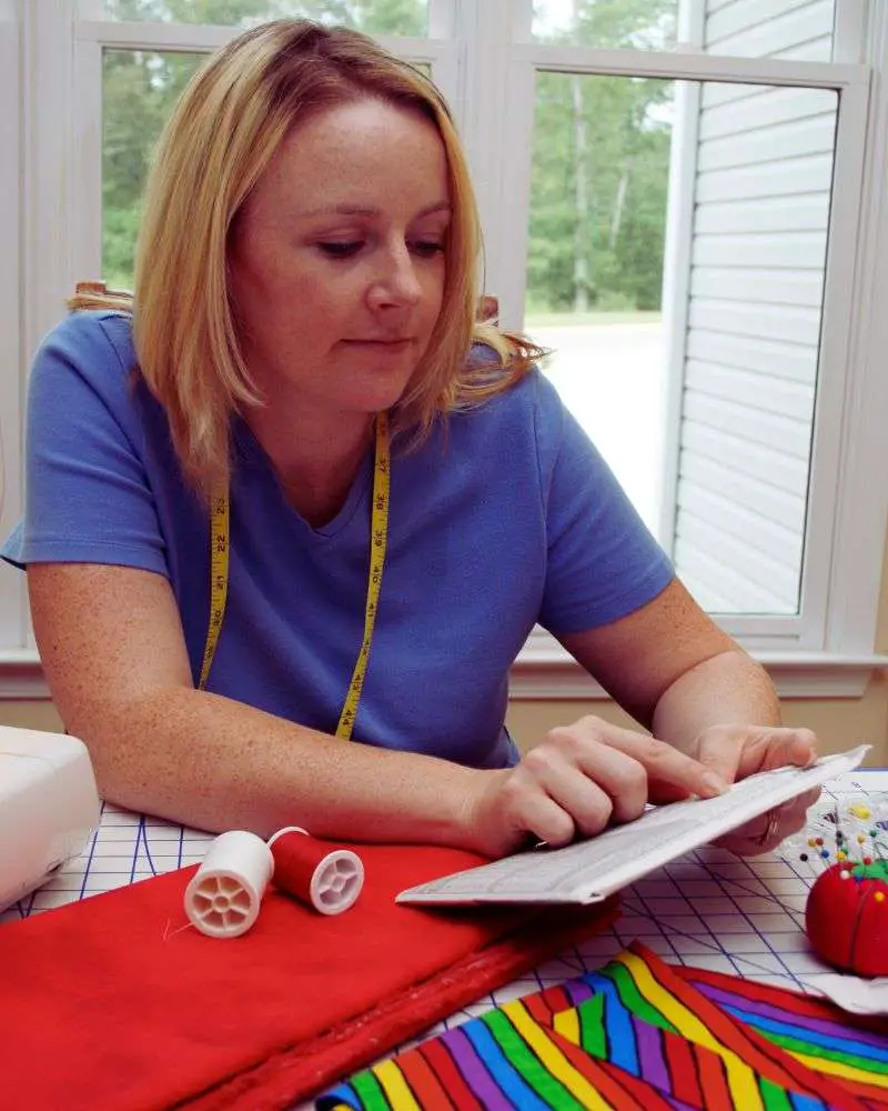 a woman sitting at a table with sewing supplies after reading 19-best-sewing-blogs-for-over-50