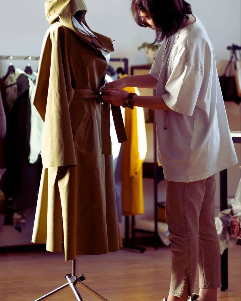 a woman measuring a coat on a mannequin