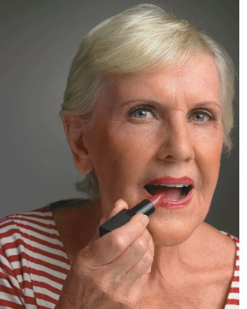 a woman putting on lipstick to demonstrate some of the best lipstick colors for over 60 women