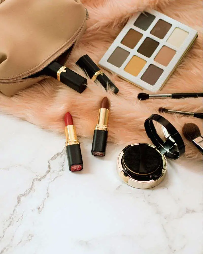 a makeup bag with lipsticks and brushes on a pink surface