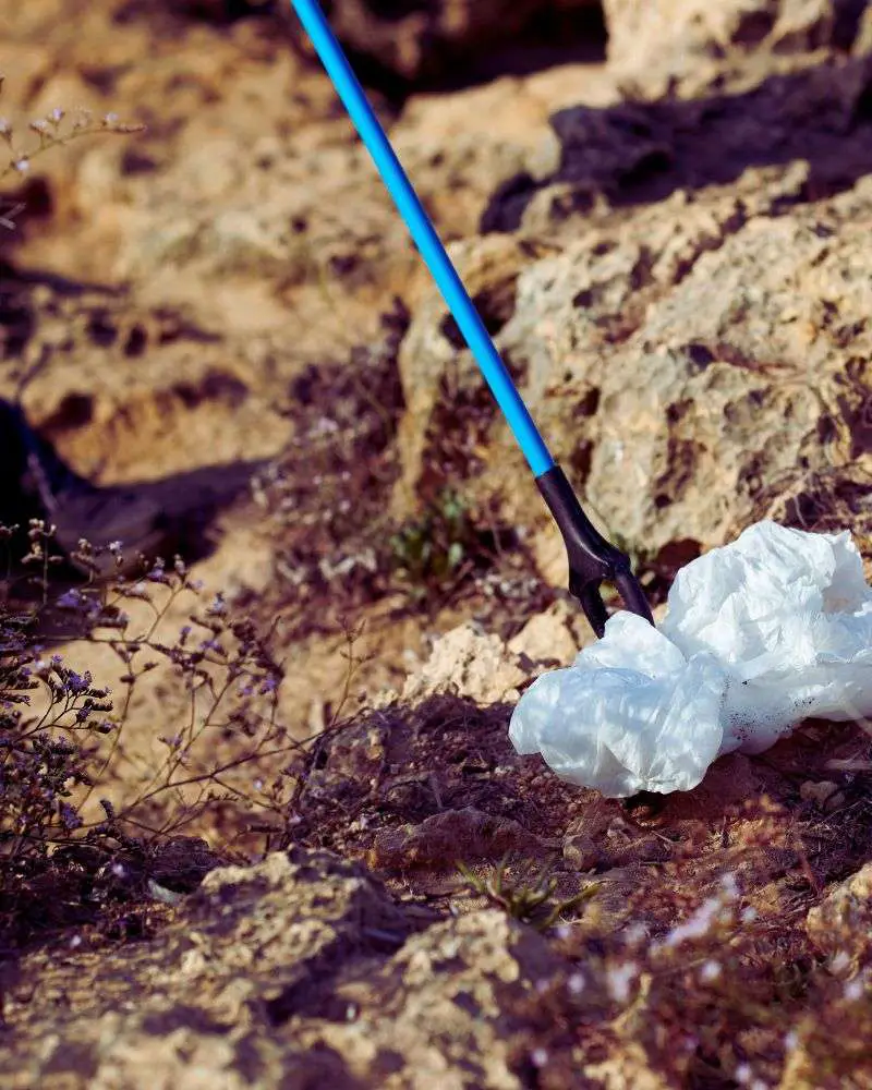 Someone using a blue grabber to pick litter off the ground