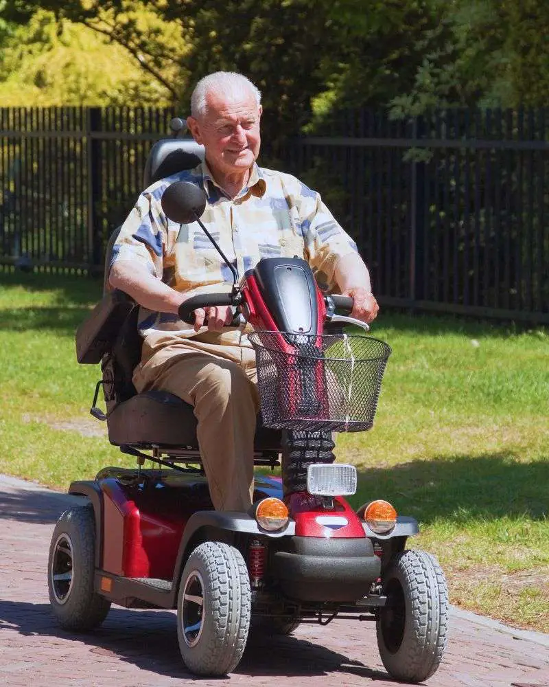 Old man riding a red scooter with a seat to demonstrate one of the many mobility devices for seniors