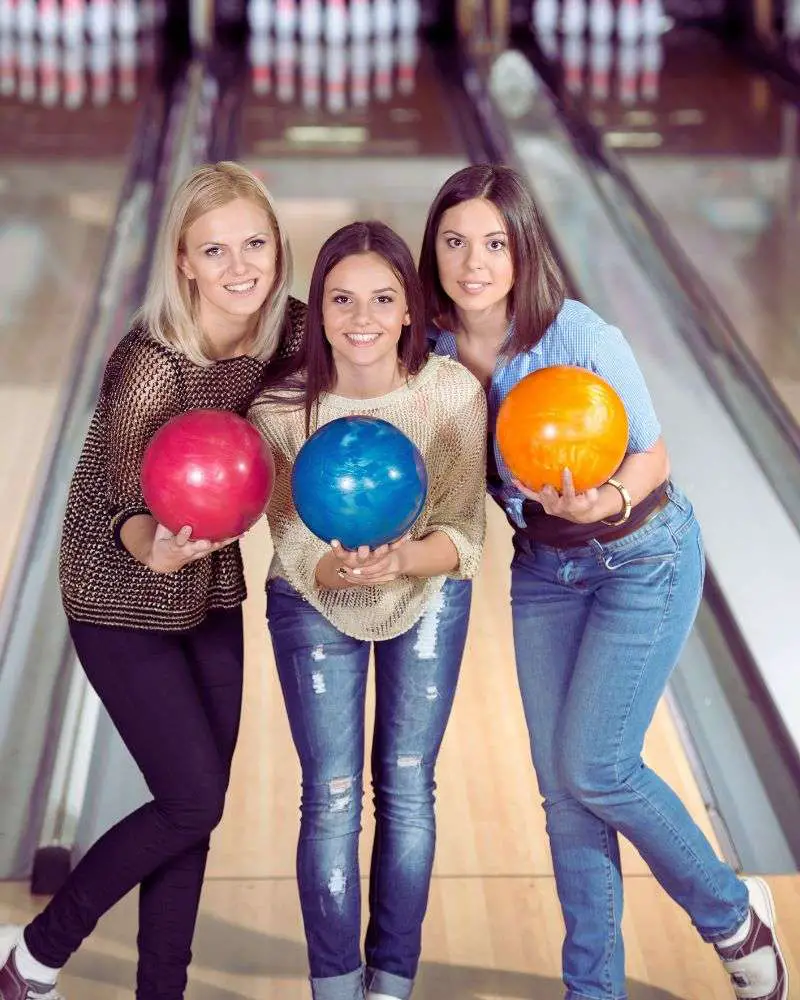 3 women holding bowling balls to demonstrate that they don't need to have the most expensive bowling balls