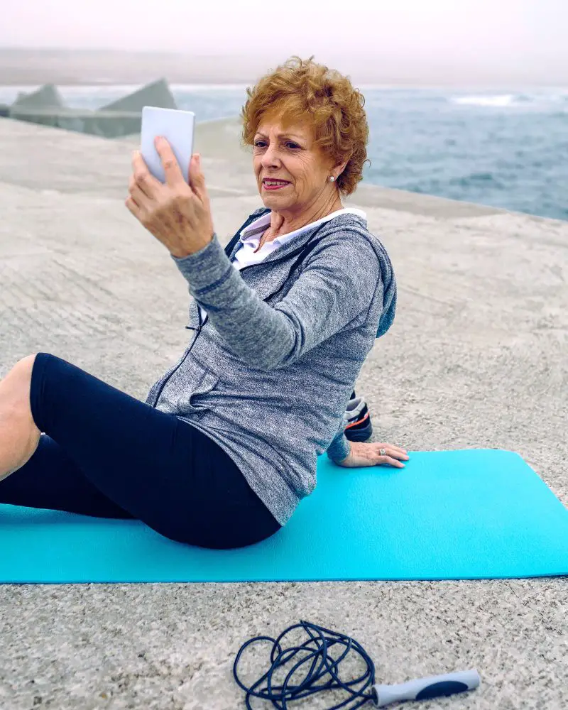 a woman sitting on a yoga mat learning how to take a good selfie over 50