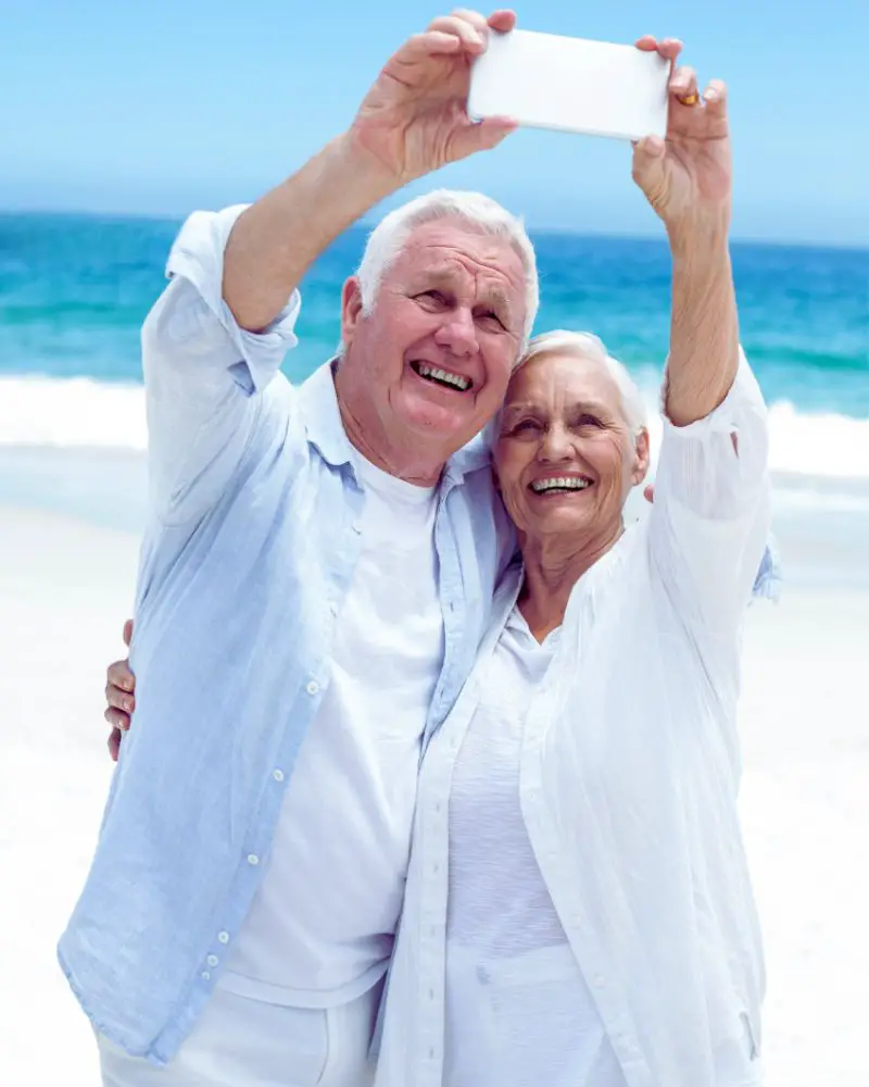 a man and woman learning how to take a good selfie over 50 on the beach