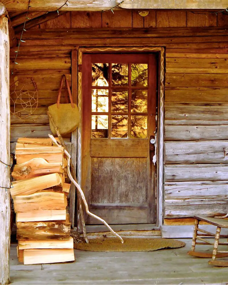 a log cabin with a wood door and a stack of logs used to convey cabin quotes for instagram