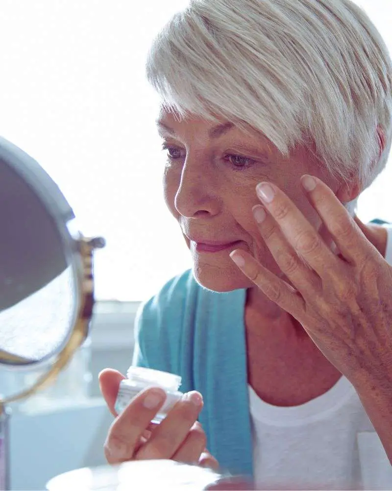 a woman applying a primer cream under her eyes after learning how to conceal under eye bags over 50