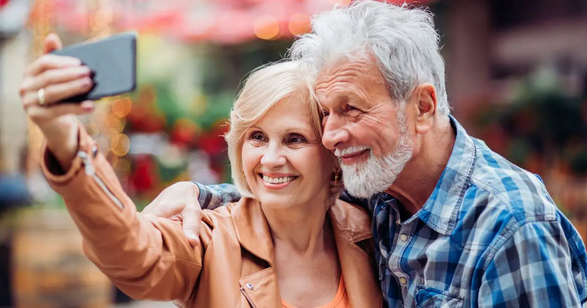 a man and woman smiling inot their phone camera as they learn how to take a good selfie over 50