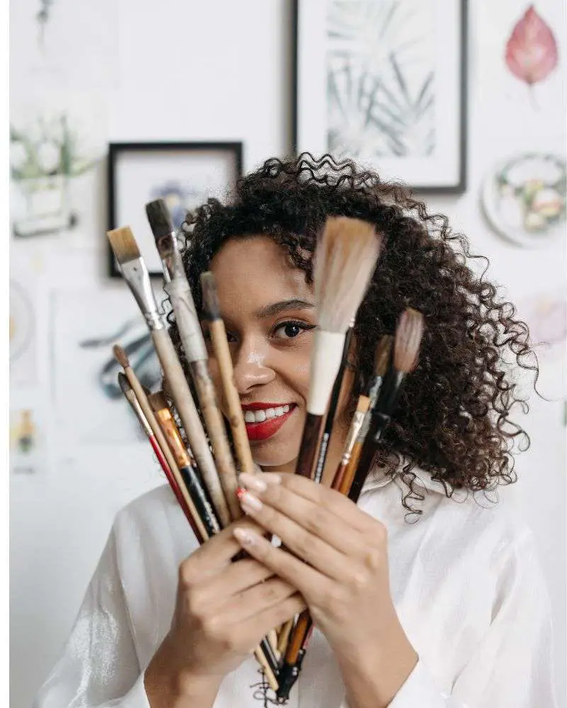 a woman holding a bunch of makeup brushes after determining the best makeup artist business names