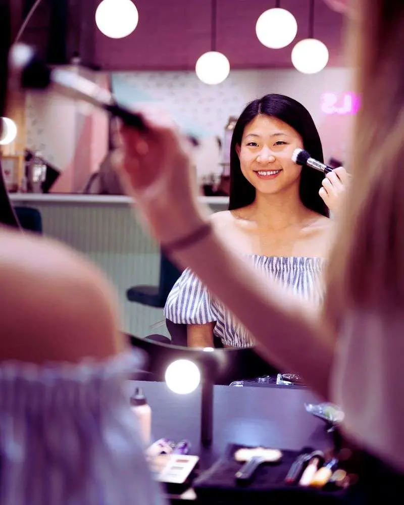 a woman putting on makeup after figuring out how to create makeup artist business names