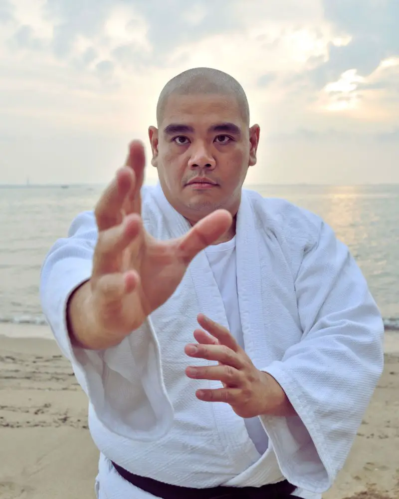 a man in a white robe on a beach performing martial arts for people over 50