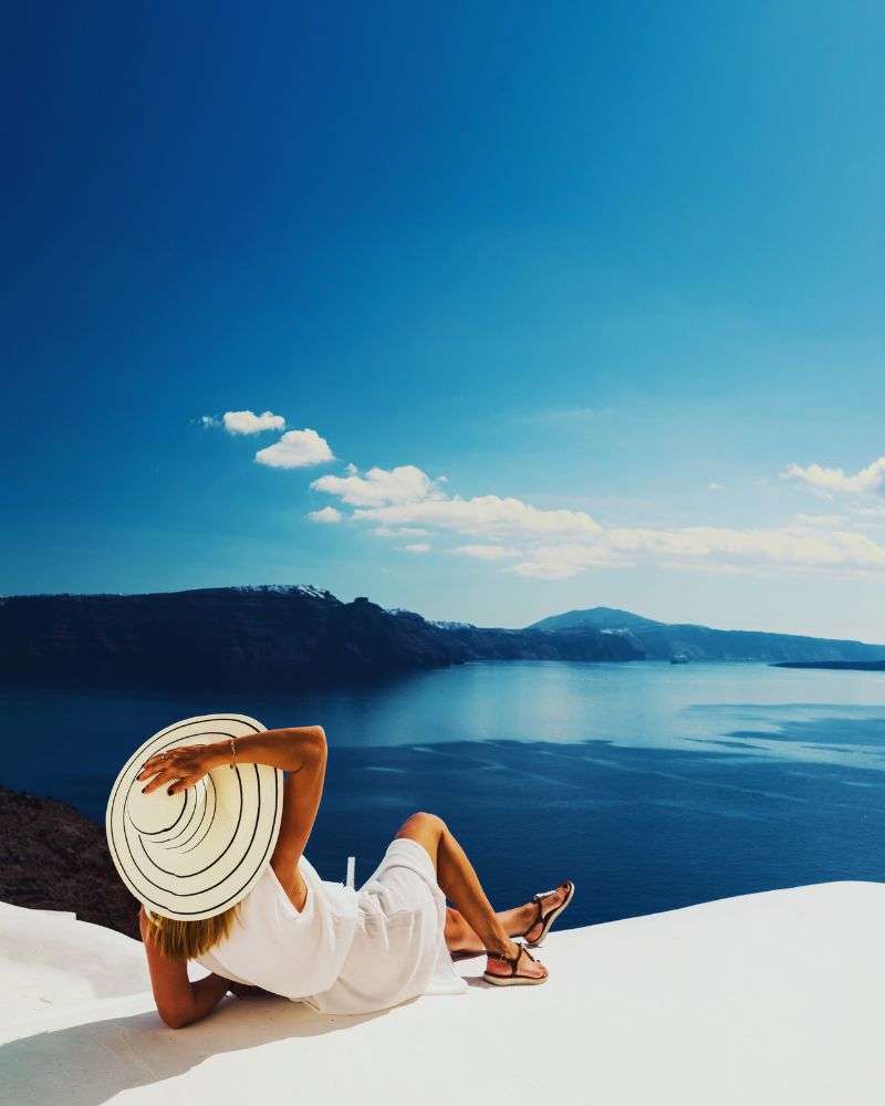 a woman in a white dress and hat sitting on a ledge by the water at one of many over 50 singles resorts