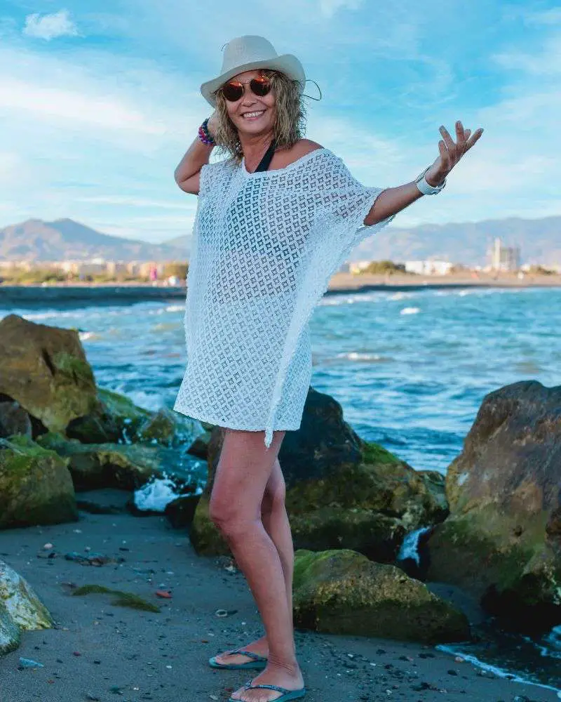 a woman wearing a white dress and hat standing on rocks by water enjoying one of many singles over 50 singles resorts