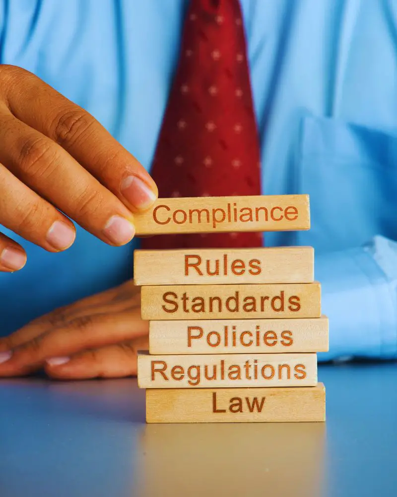 a hand stacking wooden blocks with words on them that reference selling handmade soap regulations