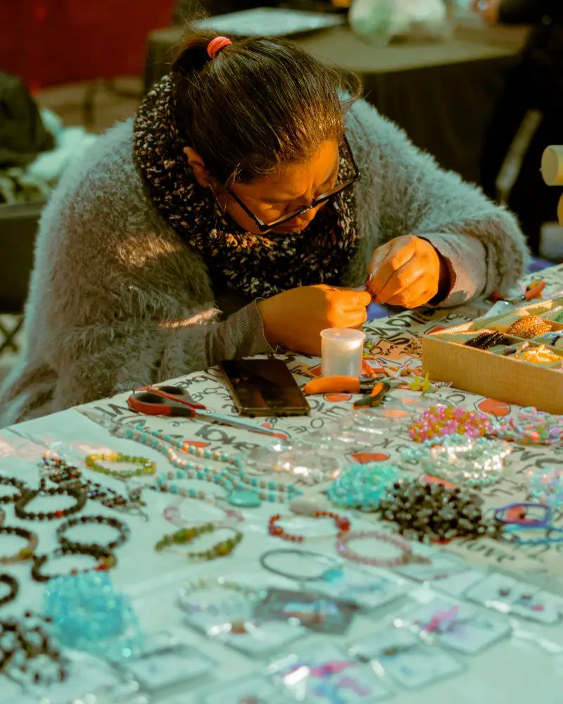 a woman making jewelry at a table to sell after learning how to turn a hobby into a side hustle