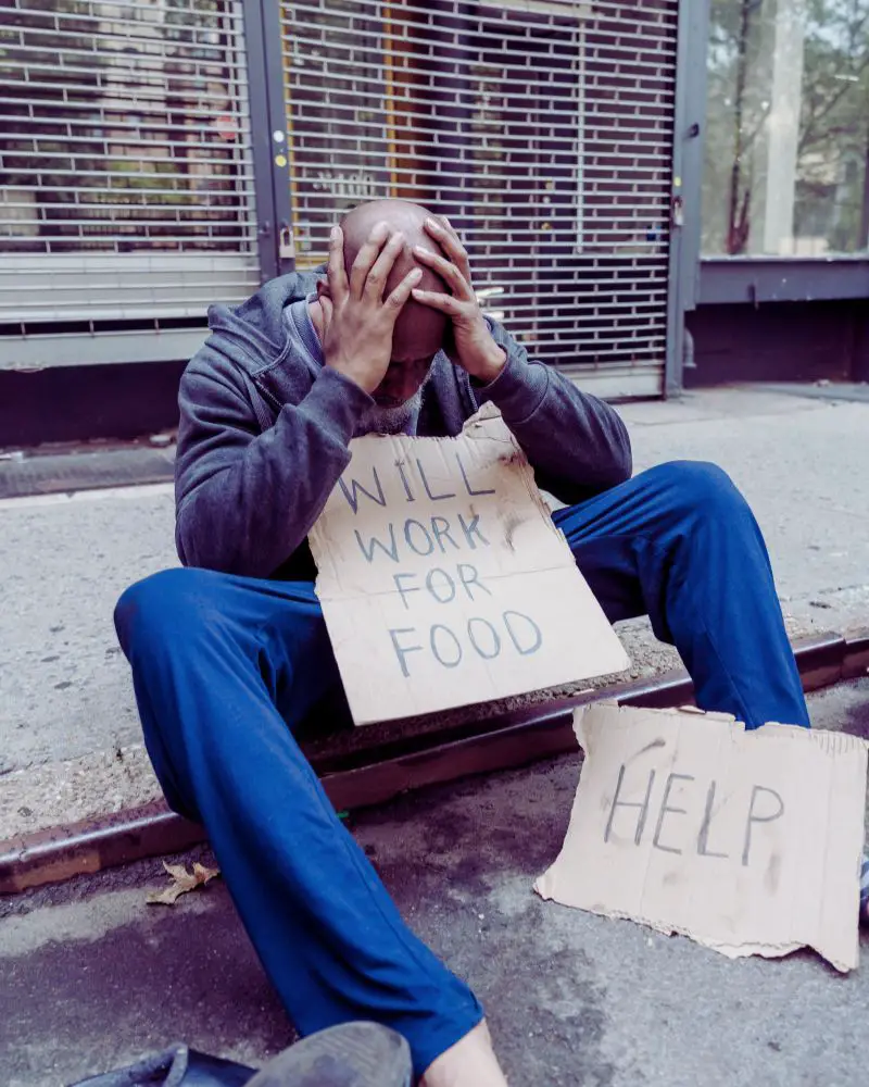 a homeless man sitting on the street holding a sign with his requests, helping to answer the question what do homeless people need?