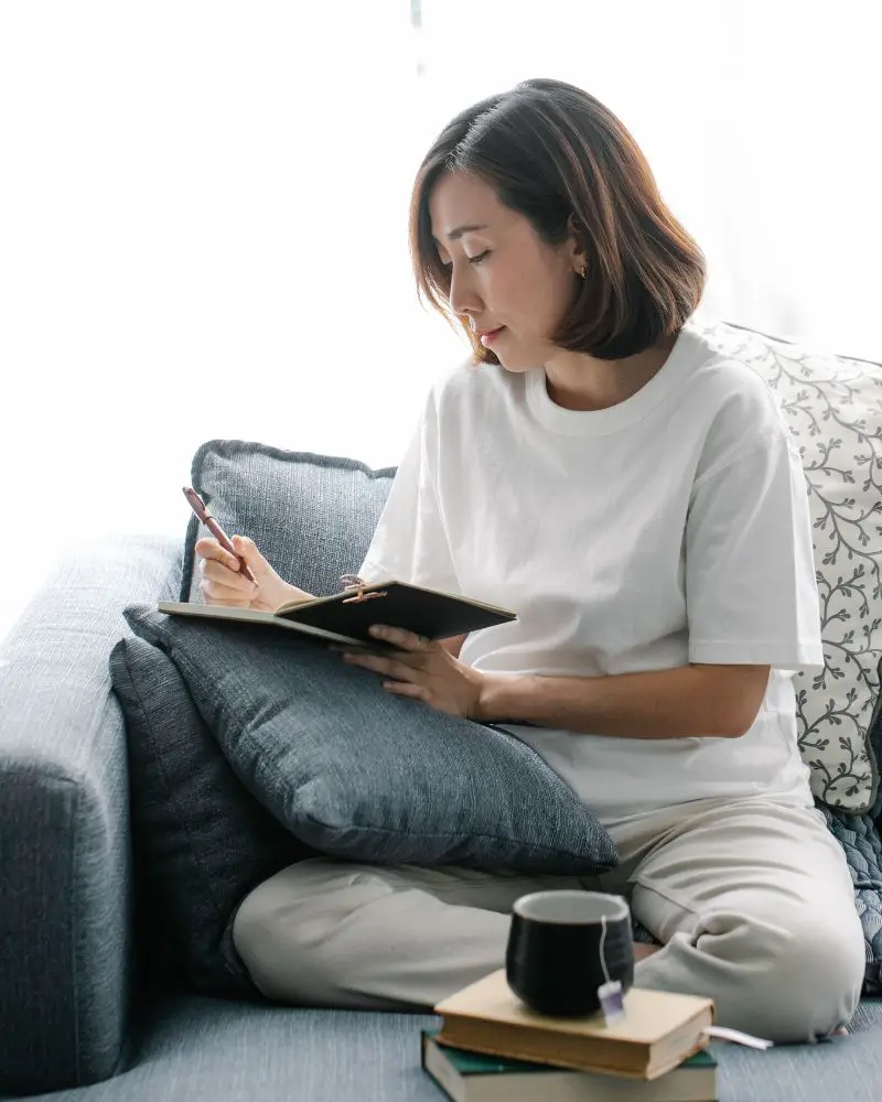 a woman sitting on a couch writing in a notebook to come up with ideas for an AI Haiku generator