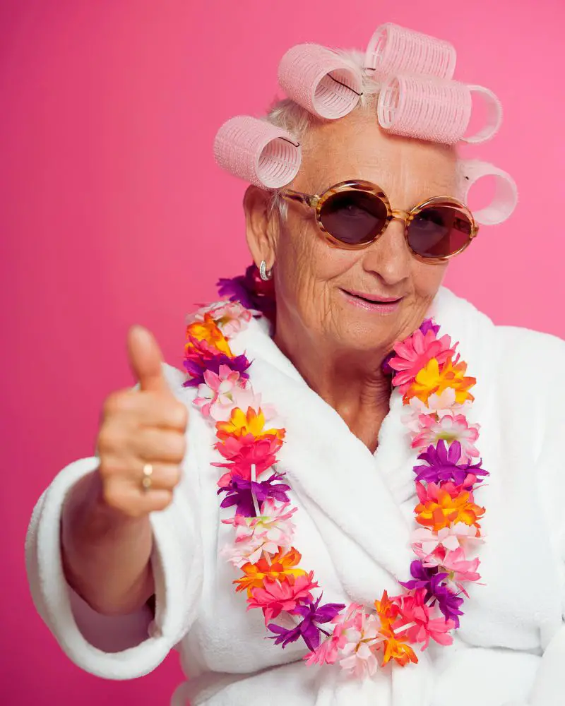 an old woman wearing sunglasses and hair rollers giving a thumbs up