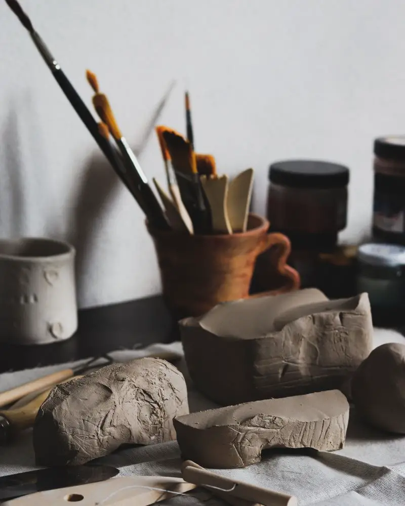 a group of clay pieces with paint brushes in the background demonstrated essential pottery studio supplies