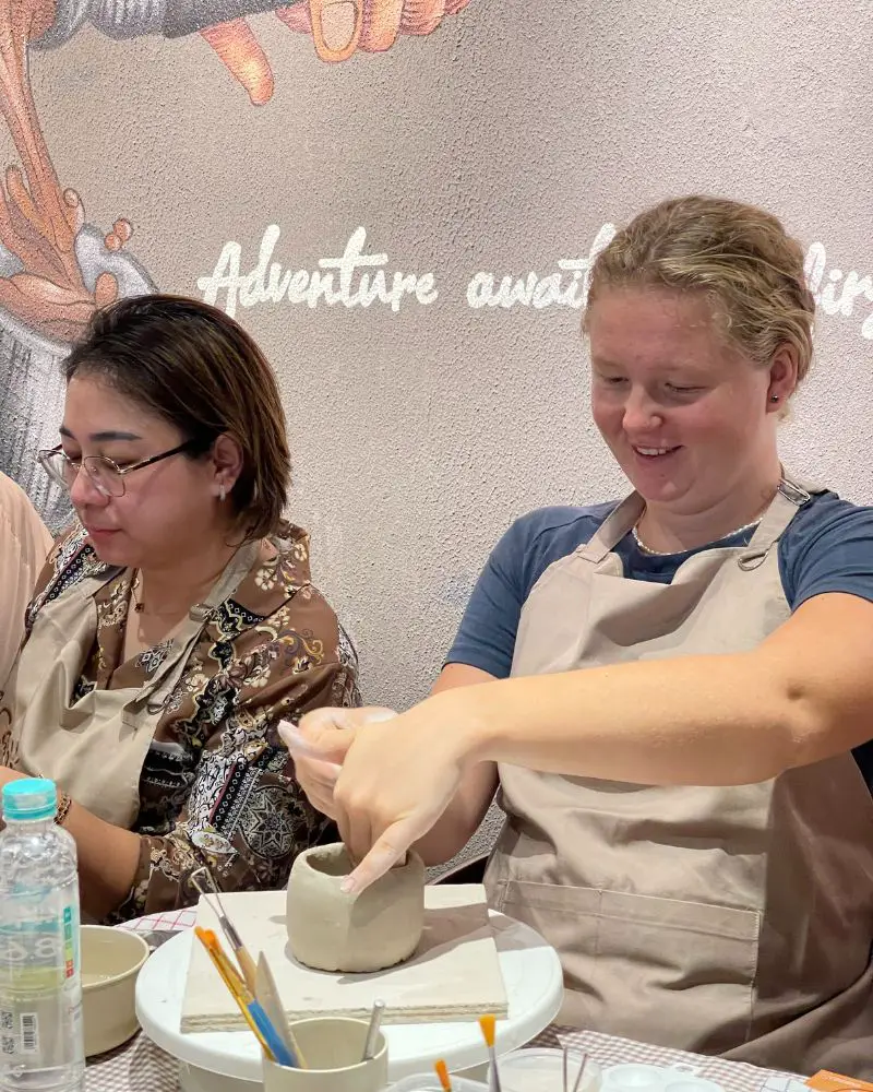 Women in aprons making a pottery cup using pottery studio supplies