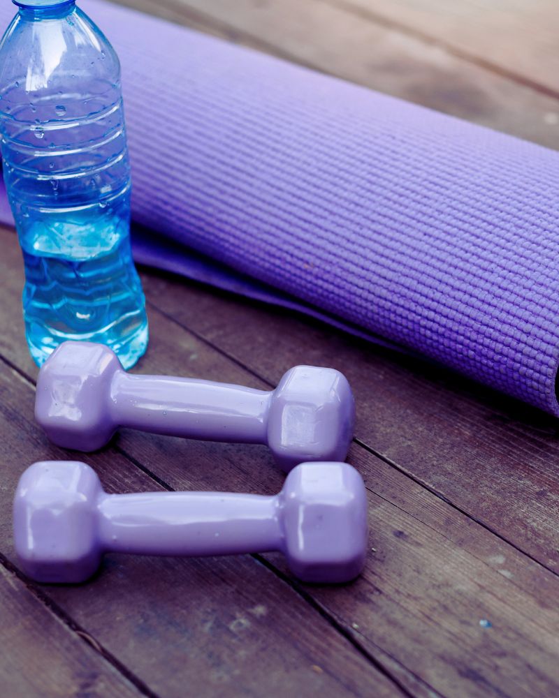 a pair of purple dumbbells next to a yoga mat to demonstrate the best exercise equipment for over 60