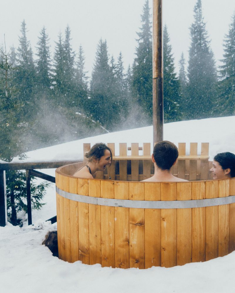 a group of people in a wooden hot tub in the snow after debating the pros and cons of a hot tub vs a pool