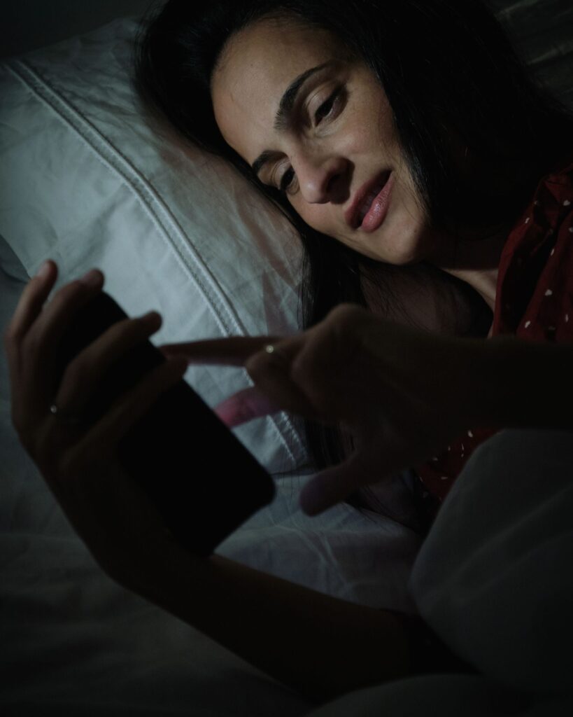 a woman lying in bed looking at a phone, which is a sign of revenge bedtime procrastination in people with ADHD