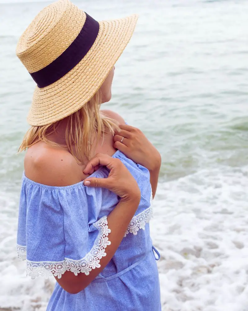 a woman wearing a hat and blue dress standing on a beach to demonstrate summer dresses for women over 50